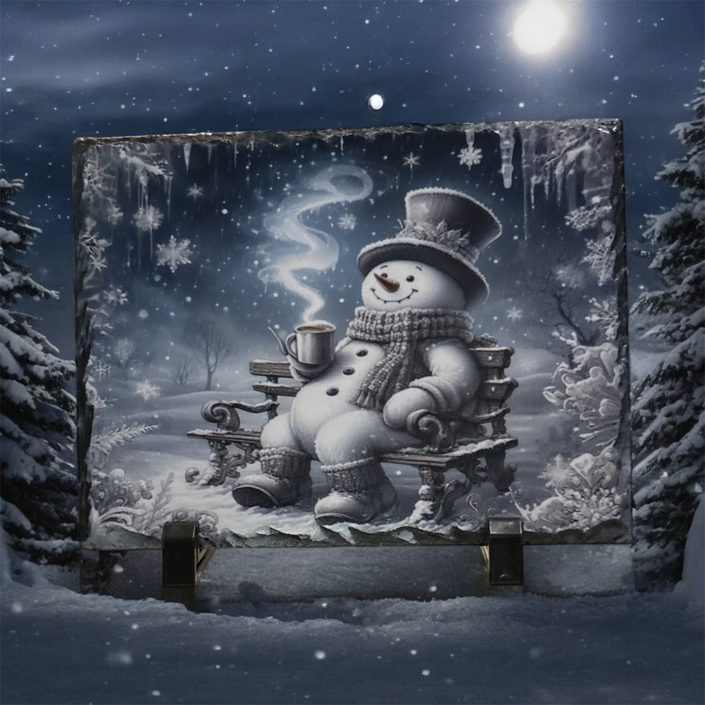 A large rectangular wall art print or canvas mounted outdoors at night, showing a snowy winter scene with a snowman sitting on a bench and holding a mug. The artwork is displayed on a support stand between snow-covered trees under a full moon.